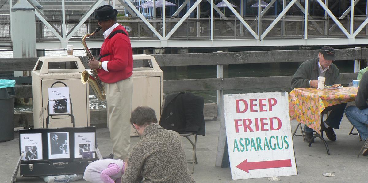 man playing saxophone near sign reading deep fried asparagus